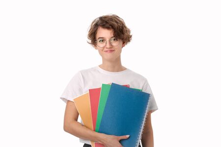 Smiling young female student in a white shirt and eyeglasses holding colorful folders isolated over white background. Concept of educationの写真素材