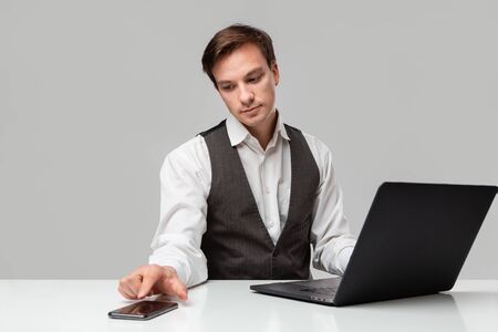 Businessman in a white t-shirt and grey vest working on a laptop. Man looking at the camera. Daily business routine.の写真素材