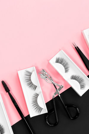 Fake eyelashes. Makeup accessories. Cosmetics. Various tools for eye lash extensions on trendy pastel pink and black background. Vertical banner. Eyelash curler, tweezers. Place for text. Top view.の写真素材