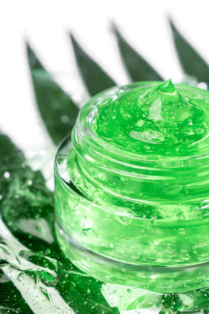 Cosmetic products for skin care and makeup. Transparent green moisturizer aloe vera gel in jar, face serum with bubble on white background with green leaves. Vertical.の写真素材