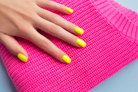 Stylish trendy female manicure. Neon yellow nails on plastic pink background. Nail polish. Art manicure. Modern style.の写真素材