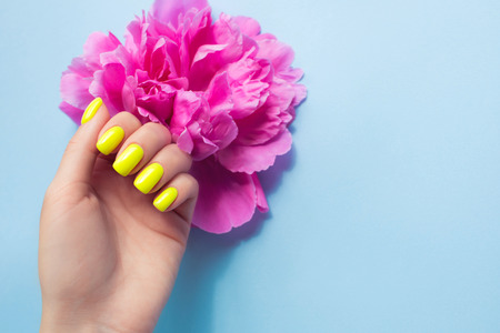 Stylish trendy female manicure. Neon yellow with pink peony flowers on blue background. Nail polish. Art manicure. Modern style.の写真素材