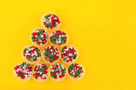 Colorful sprinkles on a yellow background making a shape of a Christmas tree. Flat lay style. Top view. Place for design.の写真素材