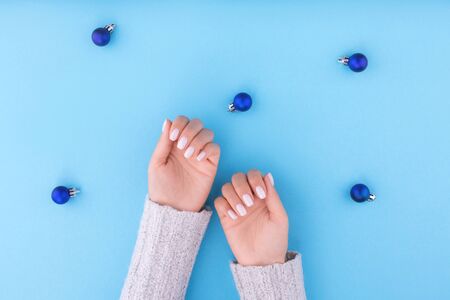 Beautiful young woman's hand with manicure on blue background with Christmas balls. Flat lay style. Top view. Place for design. Christmas composition.の写真素材