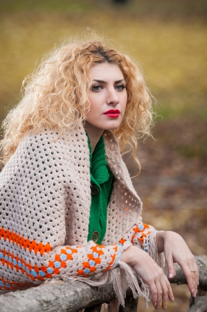 Beautiful woman posing in park during autumn season  Blonde girl wearing green blouse and big shawl posing outdoor  Long fair hair girl with green sweater under a shawl relaxing in autumnal parkの写真素材