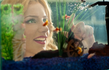 Beautiful blonde girl looking at golden fishes in aquarium  Attractive female with gorgeous smile admiring a large aquarium  Pretty woman playing with colored fishes swimming in aquariumの写真素材