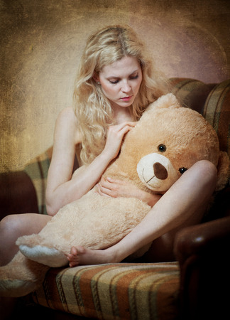 Young blond sensual woman sitting on sofa relaxing with a huge teddy bear  Beautiful girl with comfortable clothes relaxing on the couch with a toy  Attractive blonde in cosy scenery indoorの写真素材