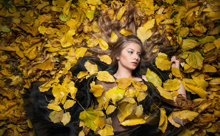  Young woman laying down on the ground covered by fall foliage in park.の写真素材