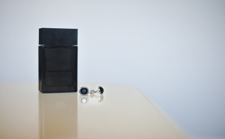 Black perfume bottle and silver cuff-links isolated on gray background. Wedding accessories.の写真素材