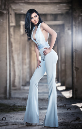 Portrait of beautiful sexy young woman with elegant overall, in urban background. Attractive young brunette with long hair and blue eyes posing fashion in white outfit. Long legs woman, side viewの写真素材