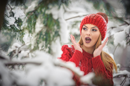 Beautiful woman in red with brown fur cape enjoying the winter scenery in forest. Blonde girl posing...