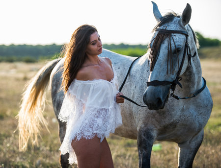 Beautiful girl with long hair posing with a white horse in the fieldの写真素材