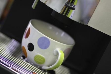 a multi colored coffee mug in a coffee dispenser ready to be filledの写真素材