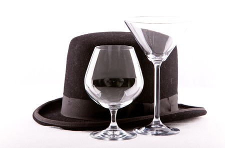 two empty wine martini or cognac glasses standing empty next to a top hat on a white backgroundの写真素材