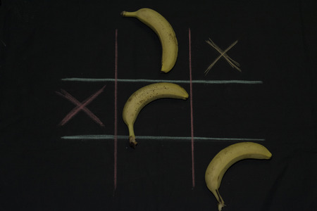 Tris Game with fruit. Three bananas on a black background. Field lines of blue and fuchsia, x boxses,の写真素材