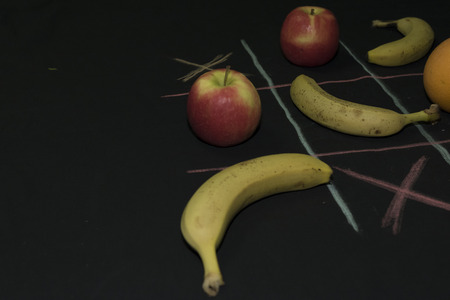 Tris Game with fruit. Three bananas, two apples and two oranges on a black background. Field lines of blue and fuchsia, x boxses, の写真素材
