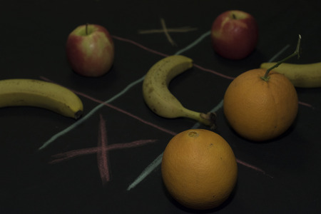 Tris Game with fruit. Three bananas, two apples and two oranges on a black background. Field lines of blue and fuchsia, x boxses,の写真素材