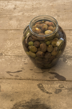 Pickled olives glass container stuffed olives preserved in liquid. Vase in the foreground, background consists of wood planks crude.の写真素材