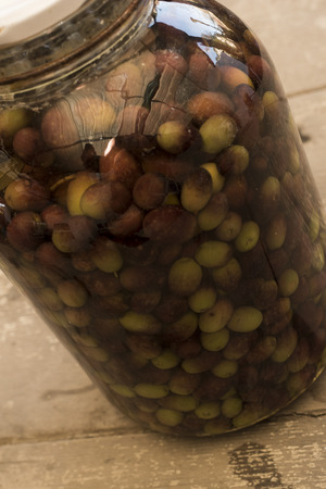 Pickled olives glass container stuffed olives preserved in liquid. Vase in the foreground, background consists of wood planks crude.の写真素材