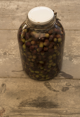 Pickled olives glass container stuffed olives preserved in liquid. Vase in the foreground, background consists of wood planks crude.の写真素材