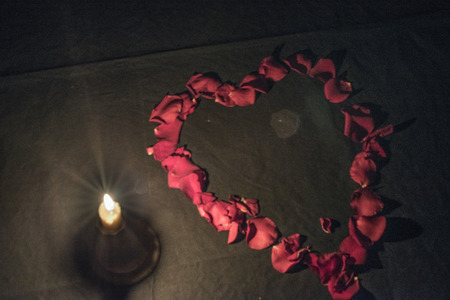 Heart of rose petals on a black background candleligthの写真素材