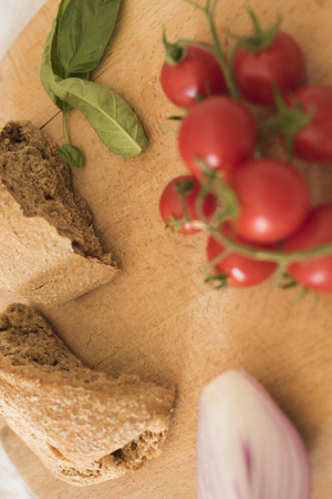 Ripe Cherry tomatoes, basil leaves, onion, hard wheat bread, arranged on wooden chopping board on white background. Ingredients Fresellaの写真素材