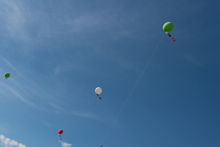 White heelium ballons, red and green, attached to wire in a blue skyの写真素材