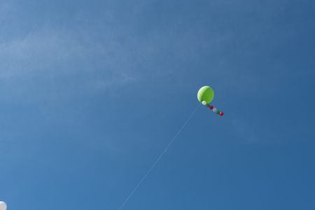 White heelium ballons, red and green, attached to wire in a blue skyの写真素材