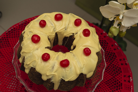 Close up of Bundt Cake with white chocolate and candied cherries on glass splashback and red crochet table centerpiece.の写真素材