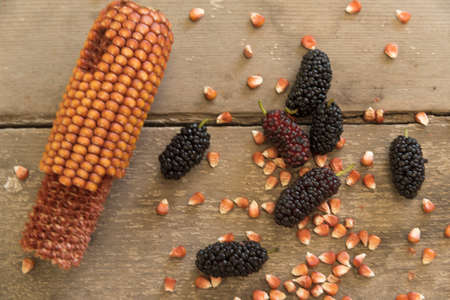 Bowl of blacks mulberry and corn kernels to pop corn on the rough wooden table.の写真素材