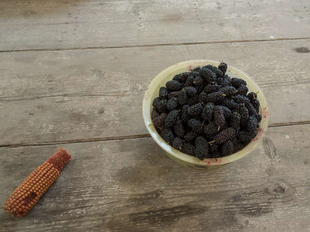 Bowl of blacks mulberry and corn kernels to pop corn on the rough wooden table.の写真素材
