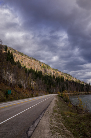 Deserted forested asphalt mountain road under a threatening overcast grey cloudy sky winding off into the distanceの写真素材