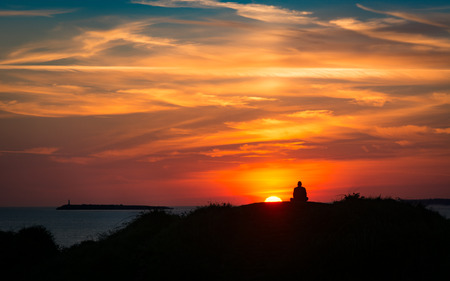 Sunset on the coast with a meditating man. Man silhouetted against a colourful sky with cloudsの写真素材