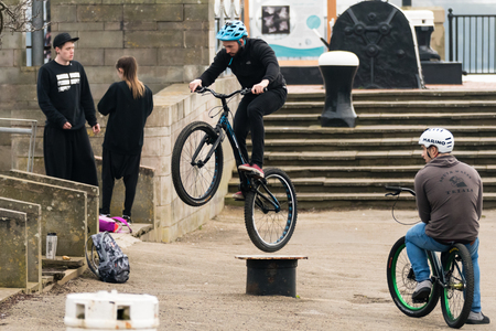 Cardiff, Wales, UK - February 18 2017: Bike riders performing tricks on street furniture. Young men make jumps for fun, with friends standing aroundのeditorial素材