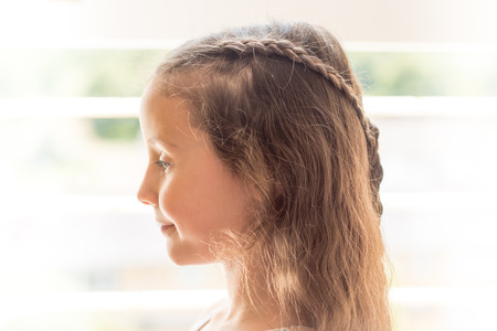 High-key portrait of girl with braided hair. Child with long brown with hairstyle with plaits, in front of windowの写真素材