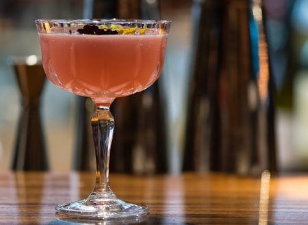 Pink cocktail garnished with flowers in Margarita glass. Alcoholic drink in tall glass on wooden...