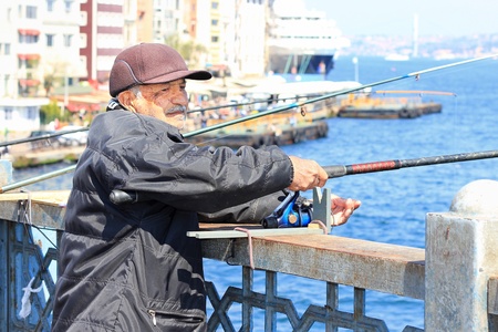 ISTANBUL - APRIL 12: An unidentified senior man fishing on Galata Bridge on April 12, 2012 in Istanbul. The bridge is well known for rod fishing in here.のeditorial素材