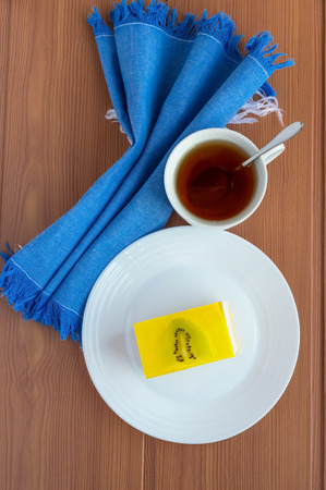 Delicate curd dessert souffle cake with jelly kiwi on a white plate on blue napkin and cup of tea.The top view.の写真素材