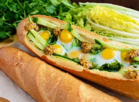 Baked crispy baguette with fried eggs, cucumbers and greens
