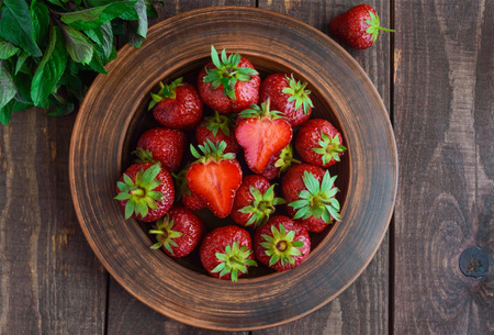 Ripe strawberries in a clay bowl, and mint leaves. On wooden background. The top viewの写真素材