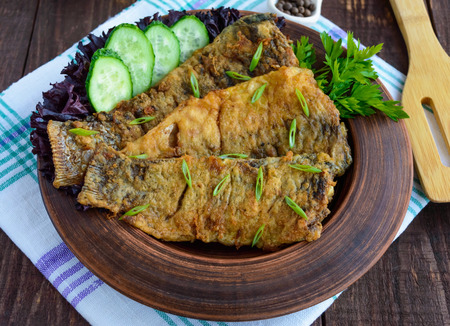 Fried carp fish fillet in batter in a clay bowl on wooden tableの写真素材