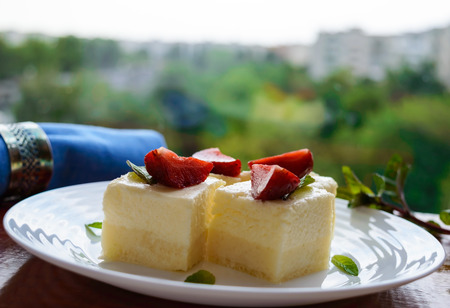 Delicate cottage cheese and creamy souffle in the form of cubes, decorating with mint leaves and fresh strawberries on a white plate on a background of natureの写真素材
