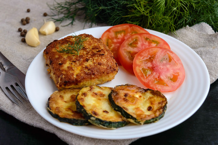Fried cutlet, tomato and zucchini on a white plateの写真素材