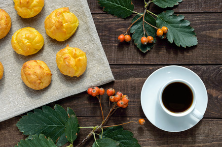 Freshly baked buns eclairs and a cup of coffee (espresso) on a dark wooden background. Light...