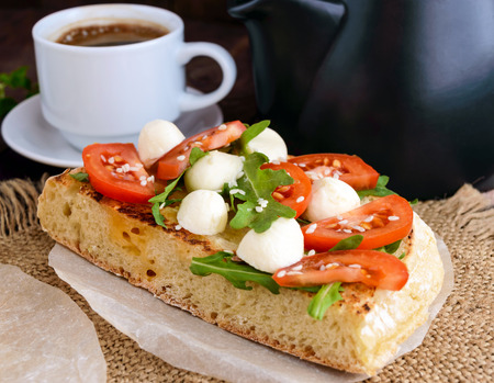 Classic sandwich with mozzarella, fresh tomatoes, arugula and sesame seeds on toast and a cup of coffee. Breakfast.の写真素材