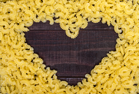 Raw macaroni - pasta Galetti.  In the middle of the empty space in the shape of a heart on a dark wooden background.の写真素材