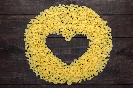 Raw macaroni - pasta Galetti.  In the middle of the empty space in the shape of a heart on a dark wooden background.の写真素材