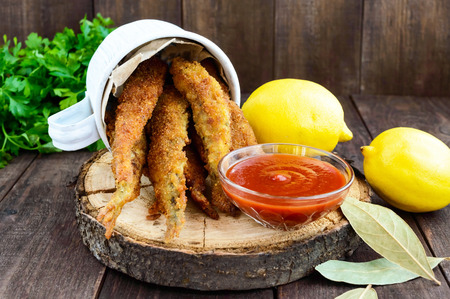 Deep frying small fish capelin in a mug on a dark wooden background. Good snack to beer.の写真素材