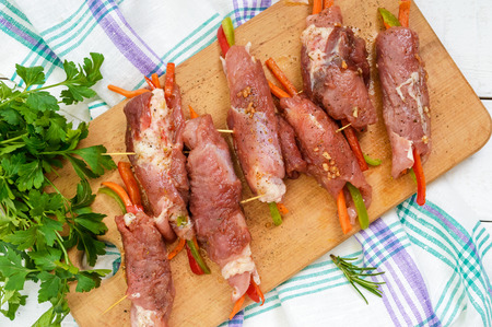 Un-cooked, pork meat rolls stuffed with vegetables (pepper, carrots) in hot garlic sauce on a cutting board. Raw, semi-finished product. The top viewの写真素材