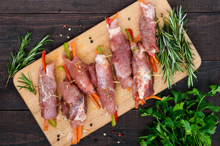 Un-cooked, pork meat rolls stuffed with vegetables (pepper, carrots) in hot garlic sauce on a cutting board. Raw, semi-finished product. The top viewの写真素材
